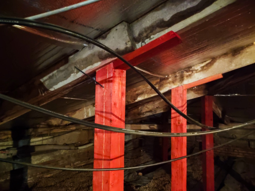 Ряд красных деревянных подпорок и кабелей под перекрытием в ремонтируемом пространстве
