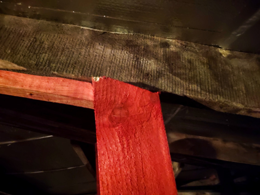 Крупный план красной деревянной стойки, подпирающей балку перекрытия под фольгированным утеплителем