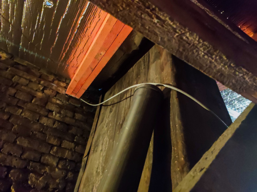 Кирпичная стена и крупная труба под перекрытием с фольгированным утеплителем и проложенным кабелем