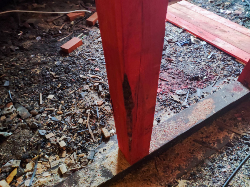 Крупный план красной деревянной стойки с повреждением у основания на фоне строительного мусора