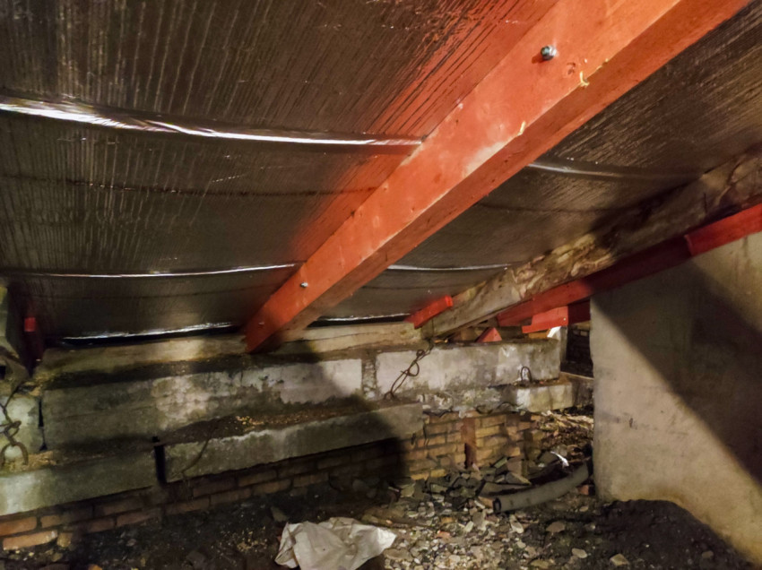 Чердак с красными балками, утеплением под кровлей и кирпичной стенкой фронтона