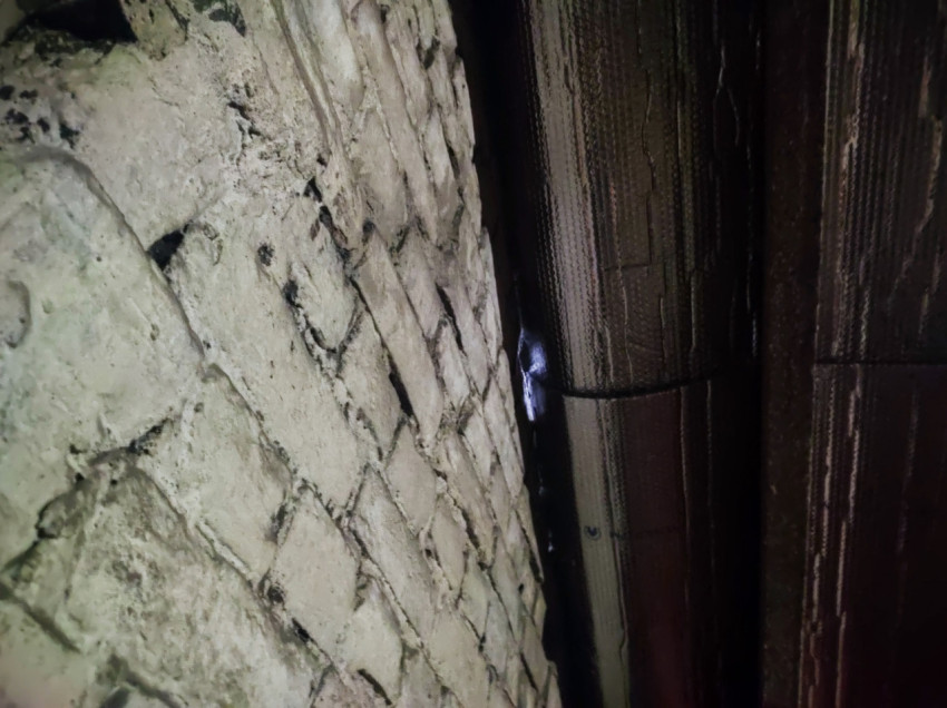 Стена из белого кирпича и тёмная подшивка крыши в узком проходе