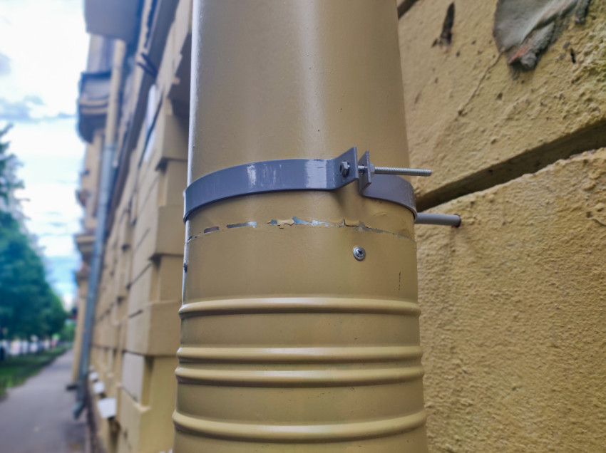 Участок водосточной трубы с хомутом на стене дома и улица на фоне