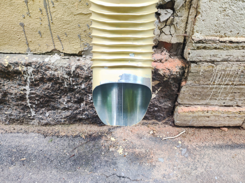 Нижний выпуск водосточной трубы с металлическим отливом у стены здания