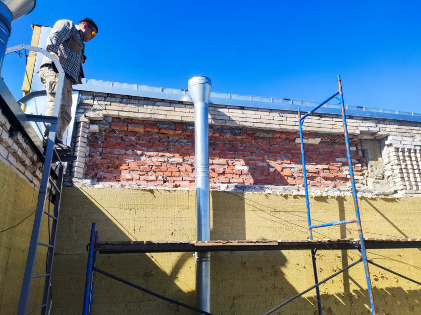 Рабочий на лестнице у кирпичной стены и строительных лесов на крыше