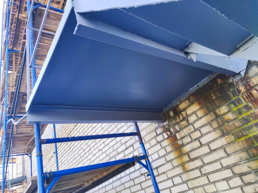 Нижняя плоскость металлической площадки у кирпичного фасада на строительных лесах