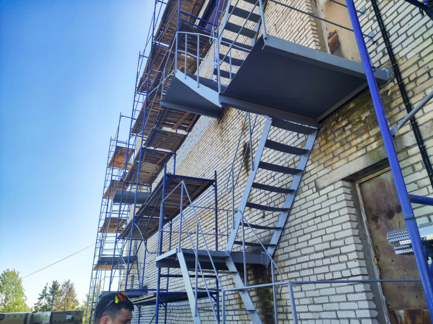 Металлическая наружная лестница и площадки на кирпичном здании рядом со строительными лесами