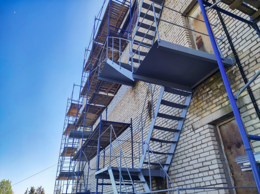 Наружная лестница с площадками на кирпичном фасаде в зоне строительных лесов