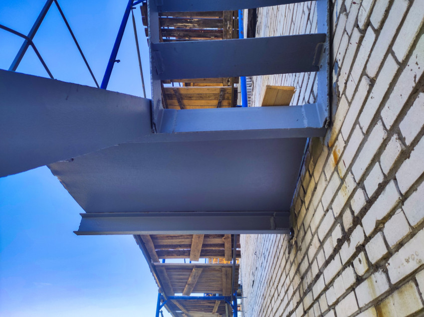 Нижняя часть металлического настила и опорные балки у кирпичной стены на лесах