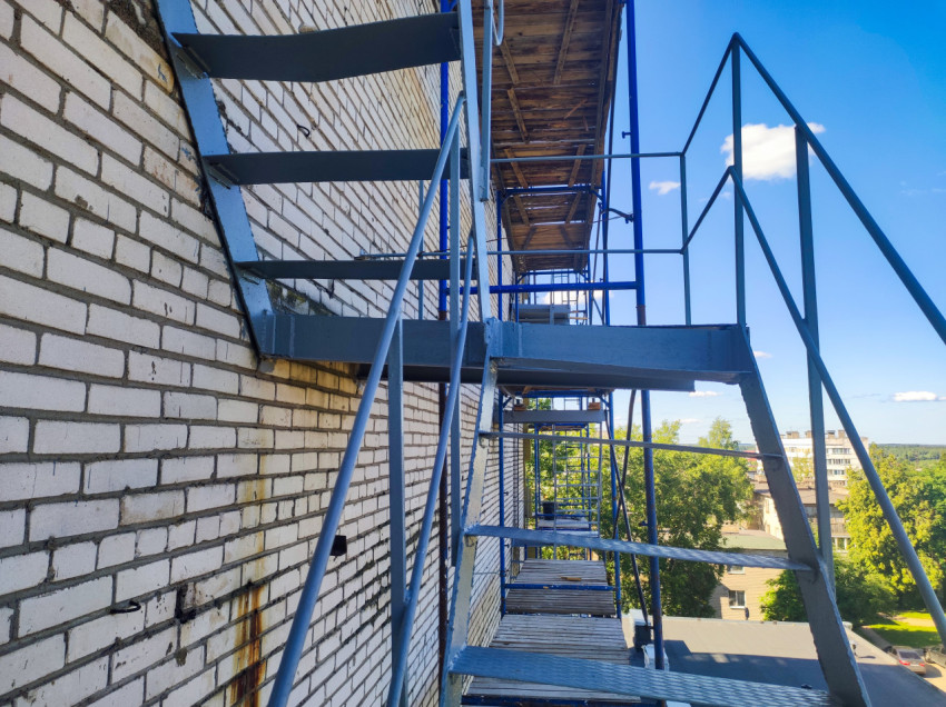 Строительные леса с металлическими балками и настилами вдоль кирпичного фасада