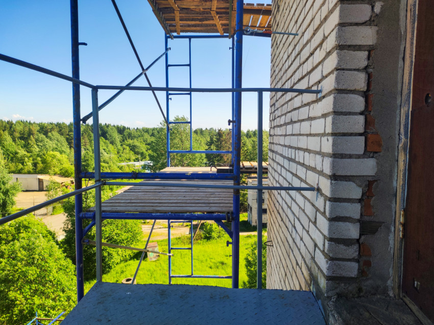 Площадка строительных лесов у кирпичного угла и металлической двери