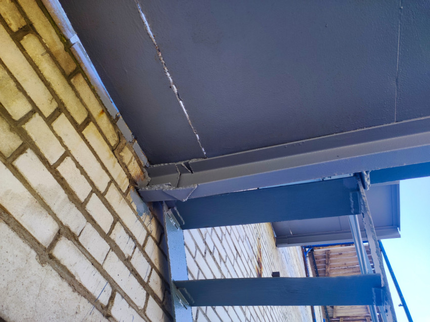 Сварной узел балки металлической площадки у кирпичной стены с видимыми швами и следами окраски