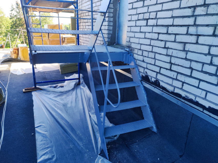 Металлическая лестница с перилами на плоской кровле рядом с кирпичной стеной и строительными лесами