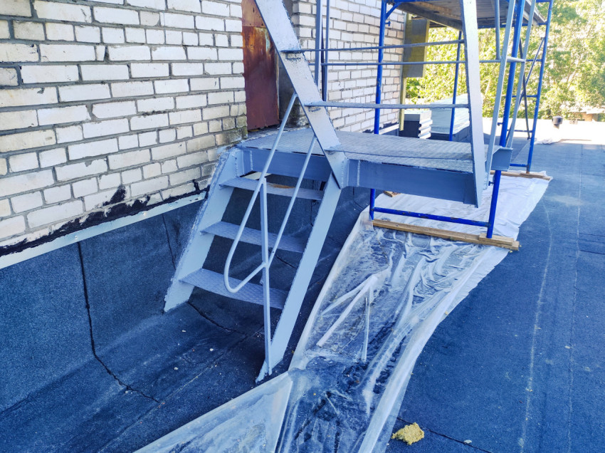 Лестница и площадка у двери надстройки на плоской кровле с временной плёнкой и строительными лесами
