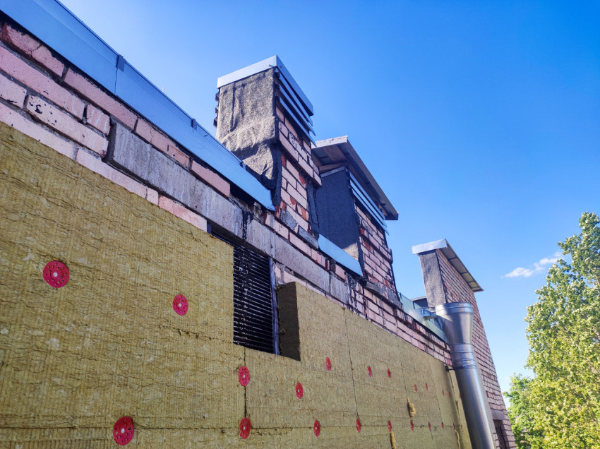 Парапет кирпичного здания с водосточными стояками, решёткой и участком утепления фасада