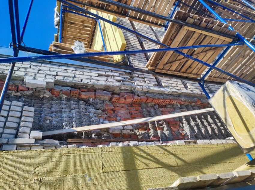 Разобранный участок кирпичной кладки под лесами при ремонте фасада и подготовке к утеплению