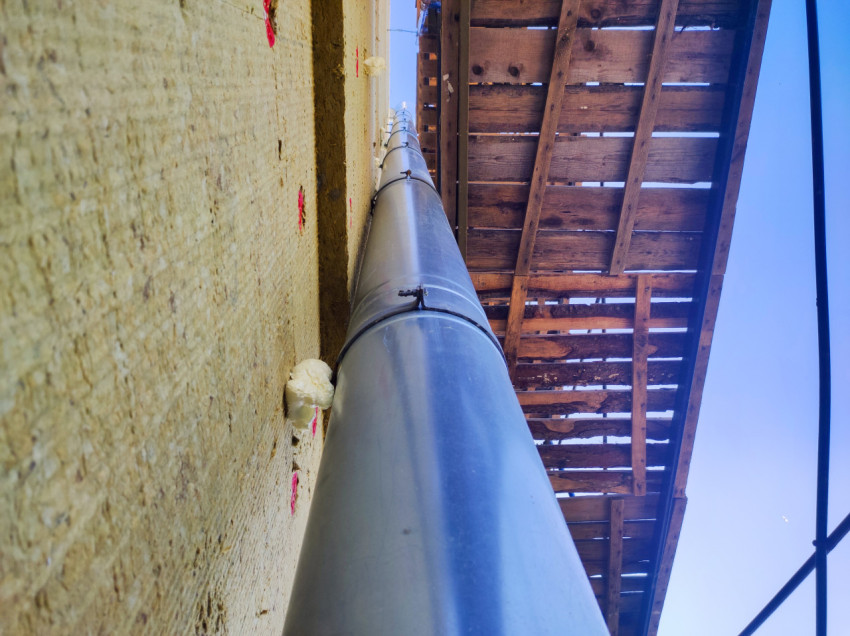 Металлическая водосточная труба на утеплённом фасаде под настилом строительных лесов, вид снизу