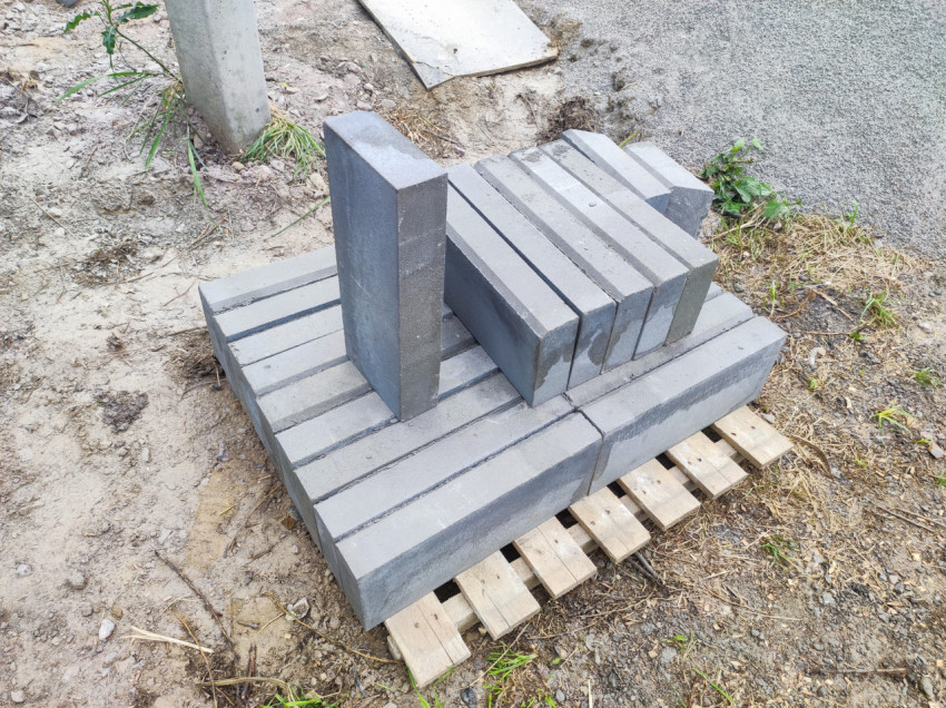Пакет серых бордюрных камней и плит на деревянном поддоне у обочины