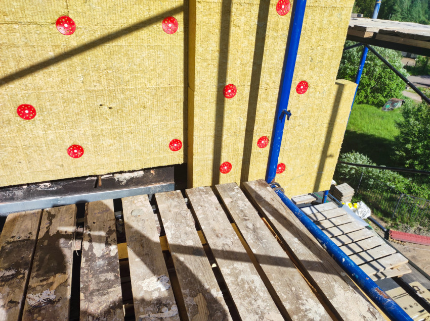 Минеральная вата с красными дюбелями и настил лесов на высоте