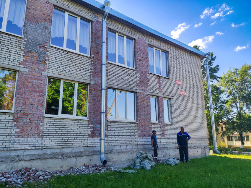 Участок кирпичного фасада с демонтированной штукатуркой и рабочими у водостока