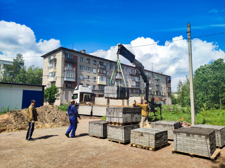Рабочие принимают поддон с бетонной плиткой при разгрузке краном-манипулятором