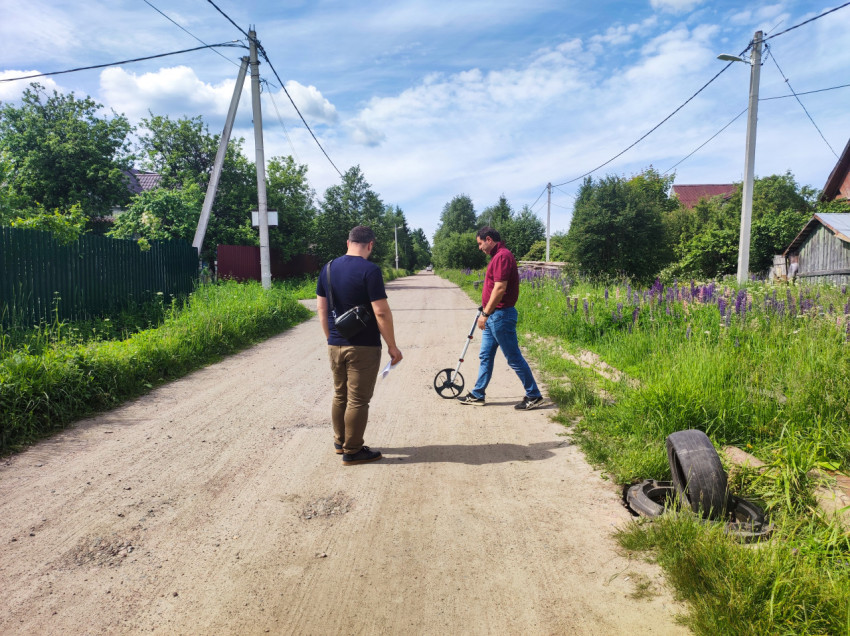 Мужчины с измерительным колесом на грунтовой дороге в частном секторе