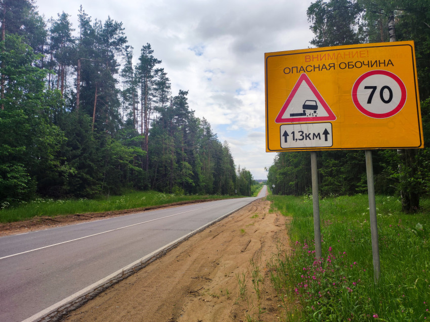Загородная дорога в лесу и предупреждающий знак об опасной песчаной обочине