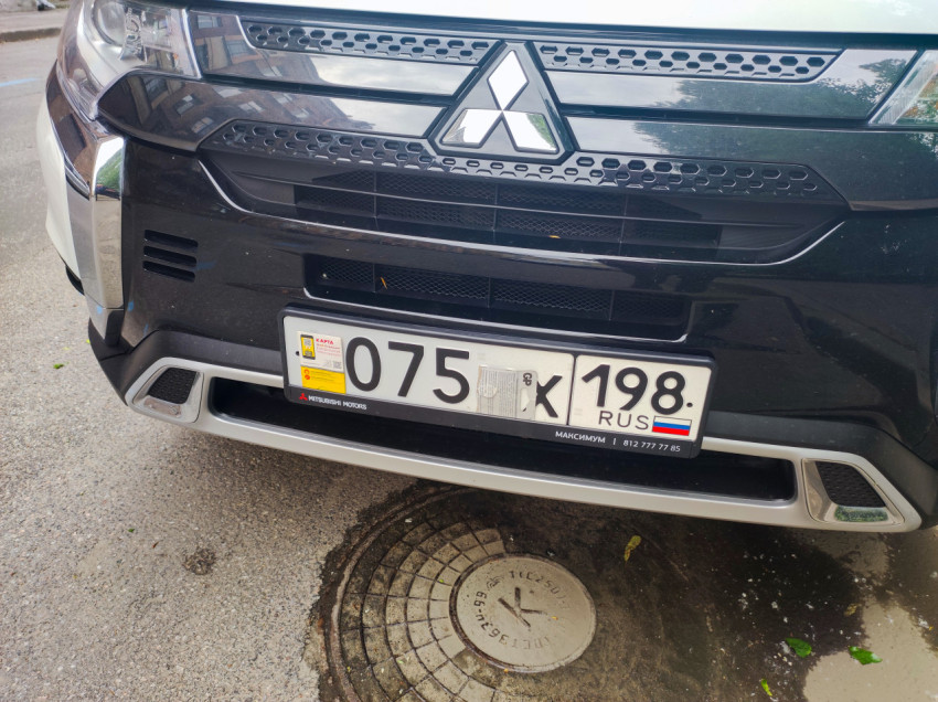 Передний бампер Mitsubishi с номерным знаком и люк на асфальте