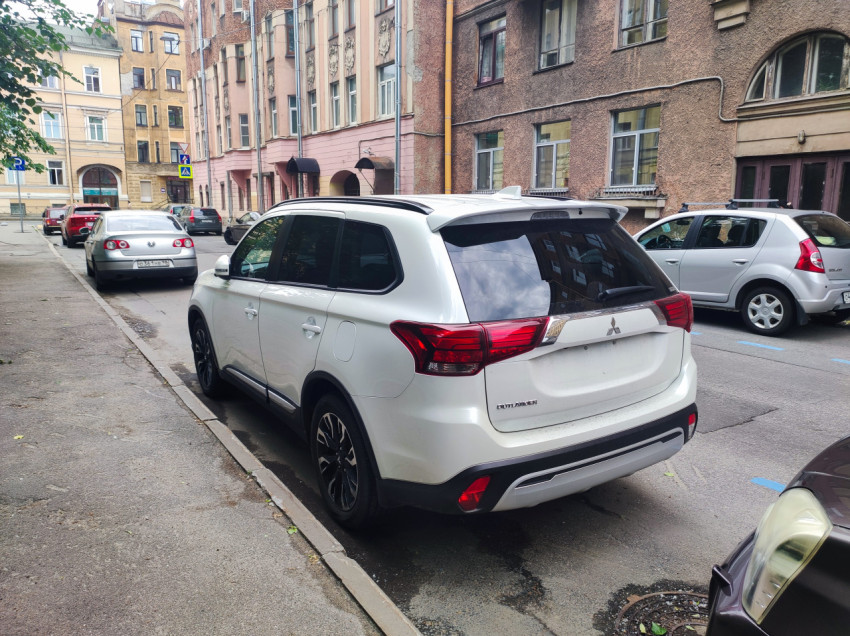 Белый Mitsubishi Outlander припаркован у тротуара на улице с жилыми домами