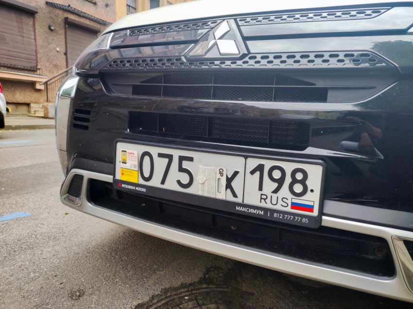 Передняя часть Mitsubishi с эмблемой и номерным знаком, номер частично закрыт