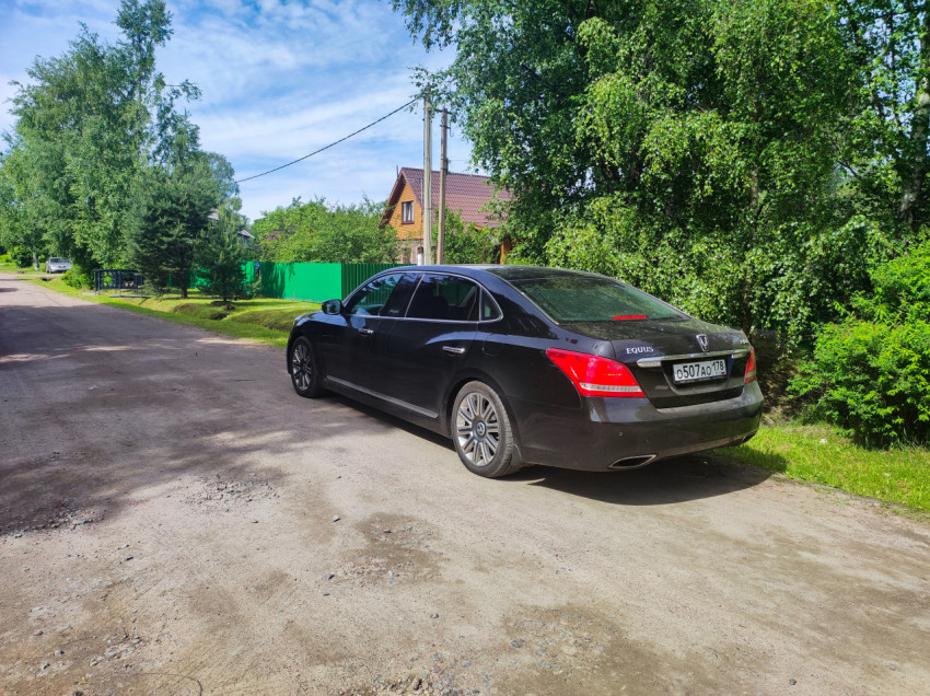 Черный седан Hyundai Equus на загородной грунтовой дороге у частных домов