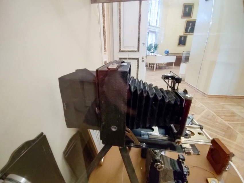 Старинный складной фотоаппарат на штативе в музейной витрине