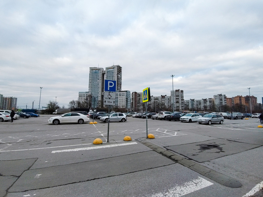 Большая парковочная зона с указателями на фоне жилых домов и высотных зданий