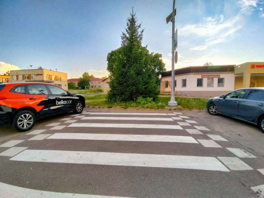 Пешеходный переход между припаркованными автомобилями рядом с магазином и аптекой