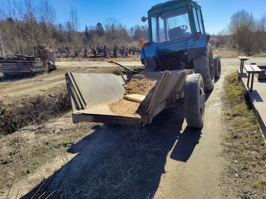 Песок в прицепе трактора на фоне захоронений