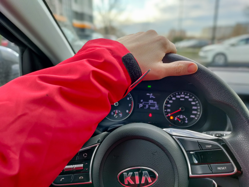 Рука водителя в красной куртке на руле автомобиля марки Kia