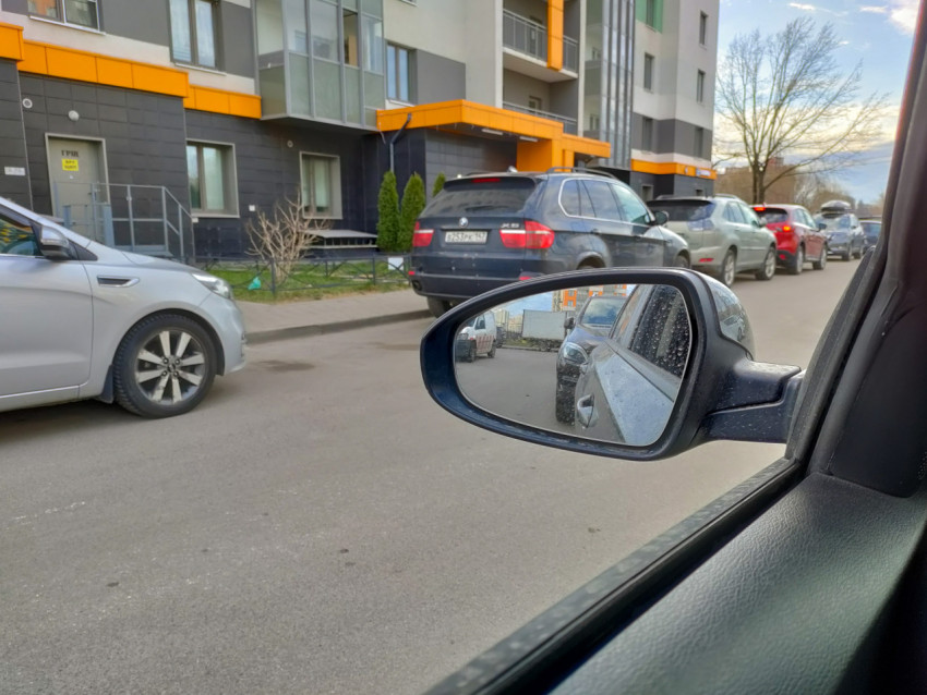 Вид на дорогу и припаркованные автомобили через боковое зеркало автомобиля