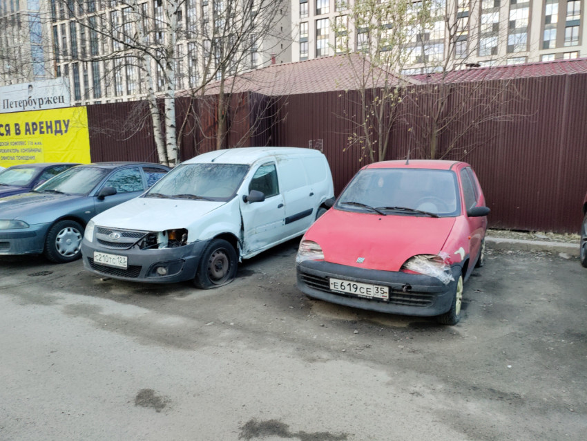 Старые повреждённые автомобили на фоне забора и жилых домов