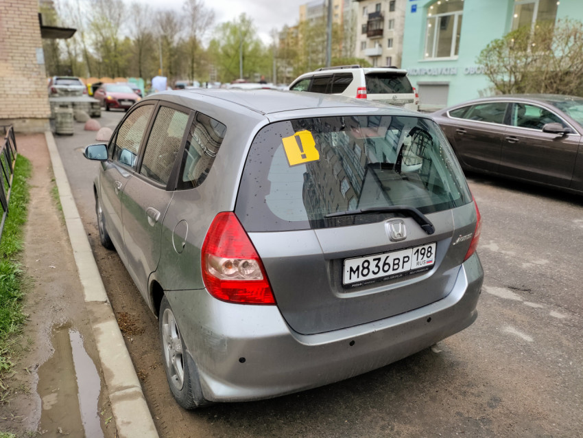 Серая Honda с наклейкой начинающего водителя на парковке