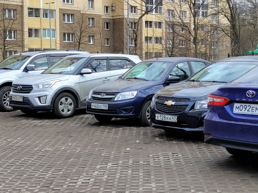 Ряд легковых автомобилей на парковке у жилого квартала