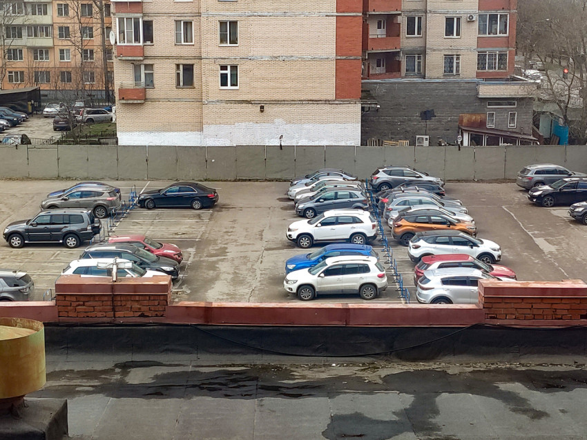 Парковка у многоэтажного жилого дома с видимыми рядами автомобилей