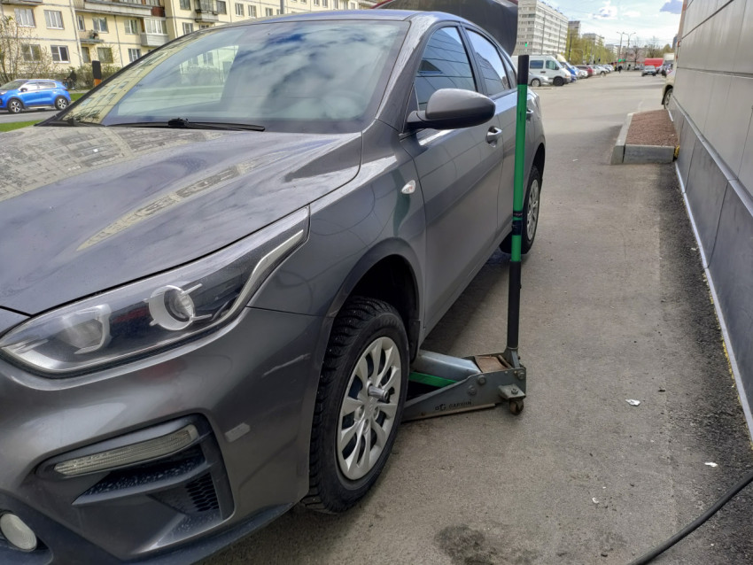 Серый автомобиль Kia на домкрате у здания