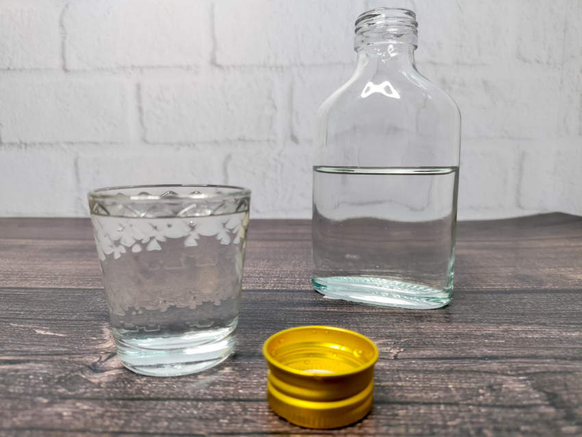 Рюмка и бутылка с прозрачной жидкостью на фоне кирпичной стены