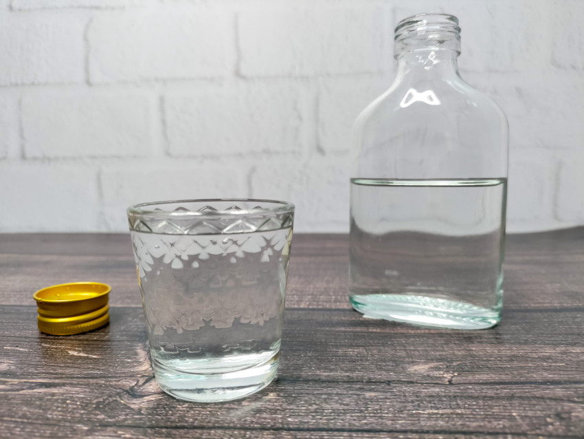 Полупустая бутылка и рюмка с прозрачным напитком на столе