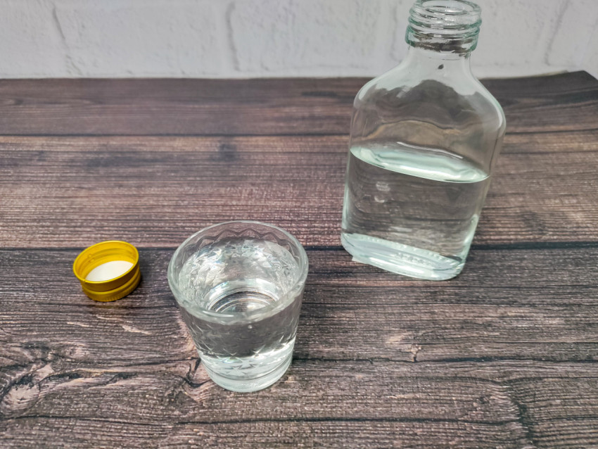 Рюмка с напитком и бутылка на фоне деревянного стола