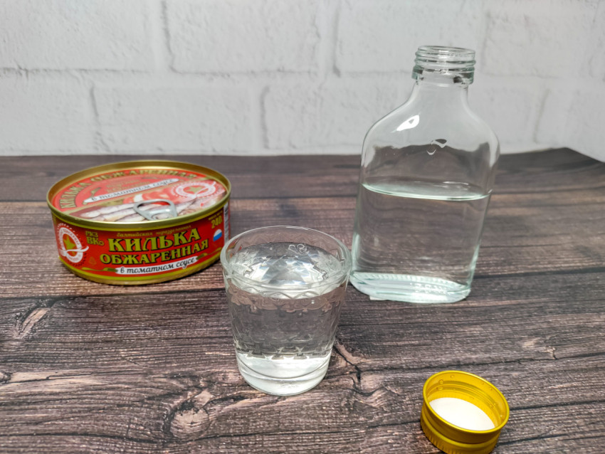 Водка, рюмка и килька в томатном соусе на столе