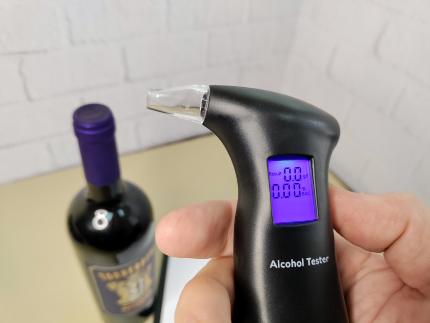Алкотестер с цифровым дисплеем и бутылка вина на фоне