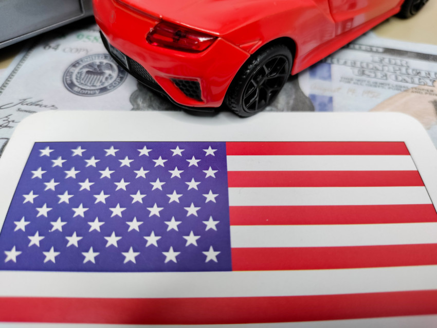 Американский флаг рядом с моделью красного автомобиля и долларовыми банкнотами
