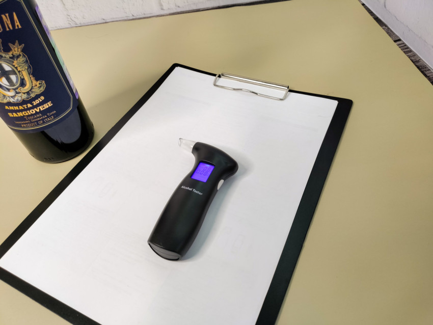 Алкотестер на столе рядом с бутылкой вина и документами