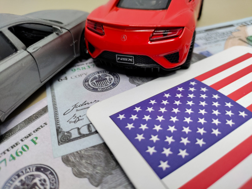 Красный и серебристый автомобили на фоне флага США и долларов